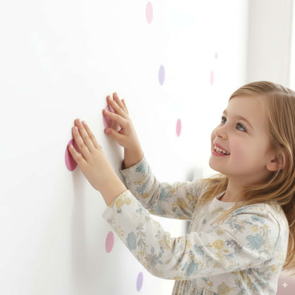 Gros plan sur une petite fille qui applique un sticker pois rose bonbon, montrant la facilité d'installation de ces stickers muraux pour la chambre d'enfant.