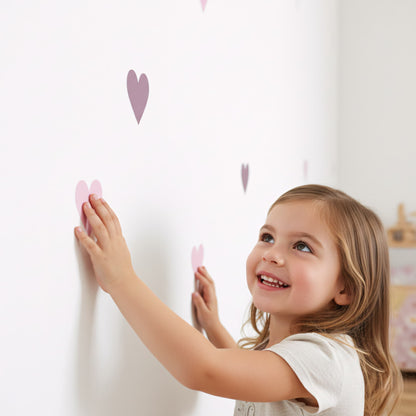 Une petite fille souriant pose des stickers coeurs teintes violet sur le mur