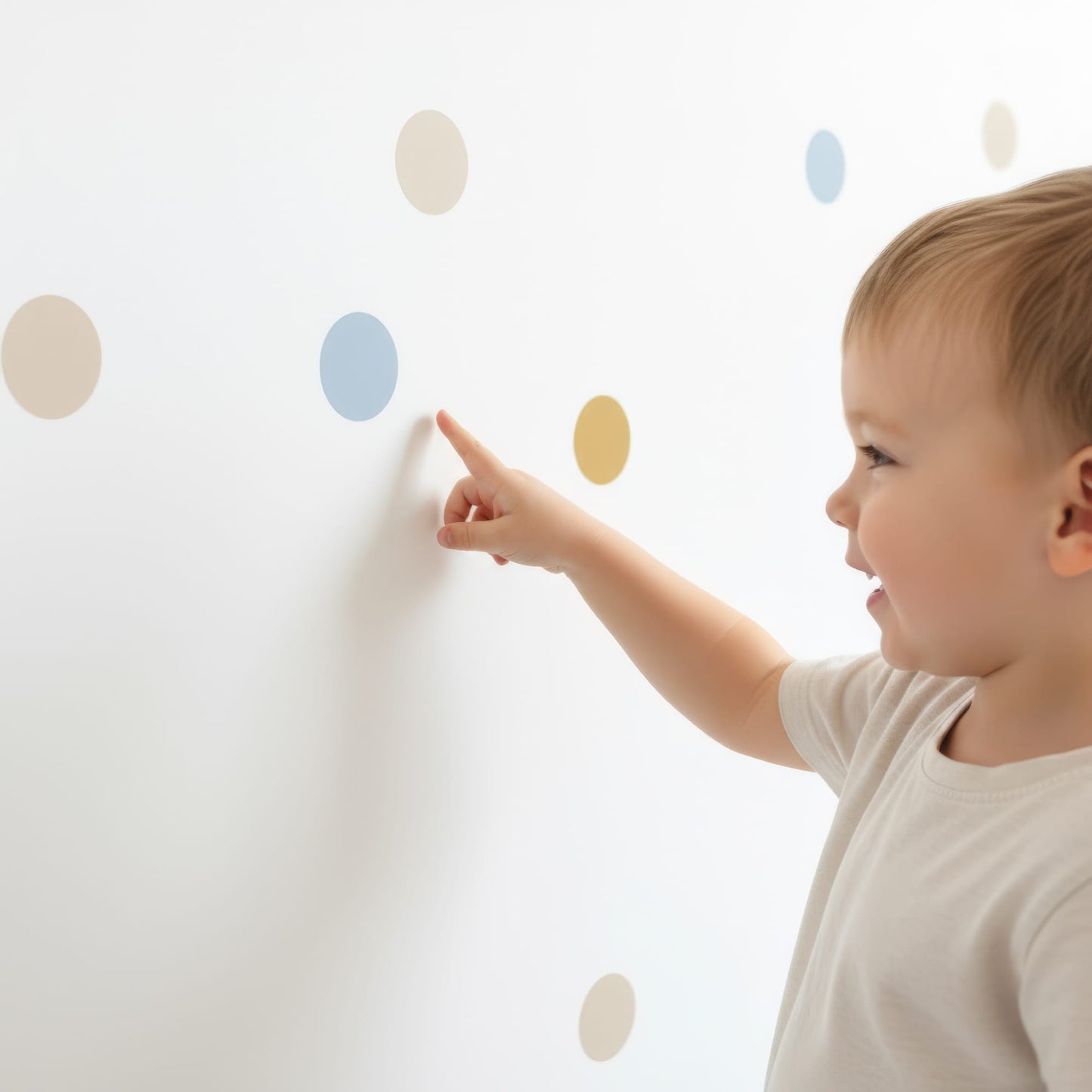Un jeune enfant souriant pointe du doigt un sticker pois bleu doré sur un mur, mettant en avant la facilité d'utilisation de cette décoration murale pour chambre enfant et bébé.