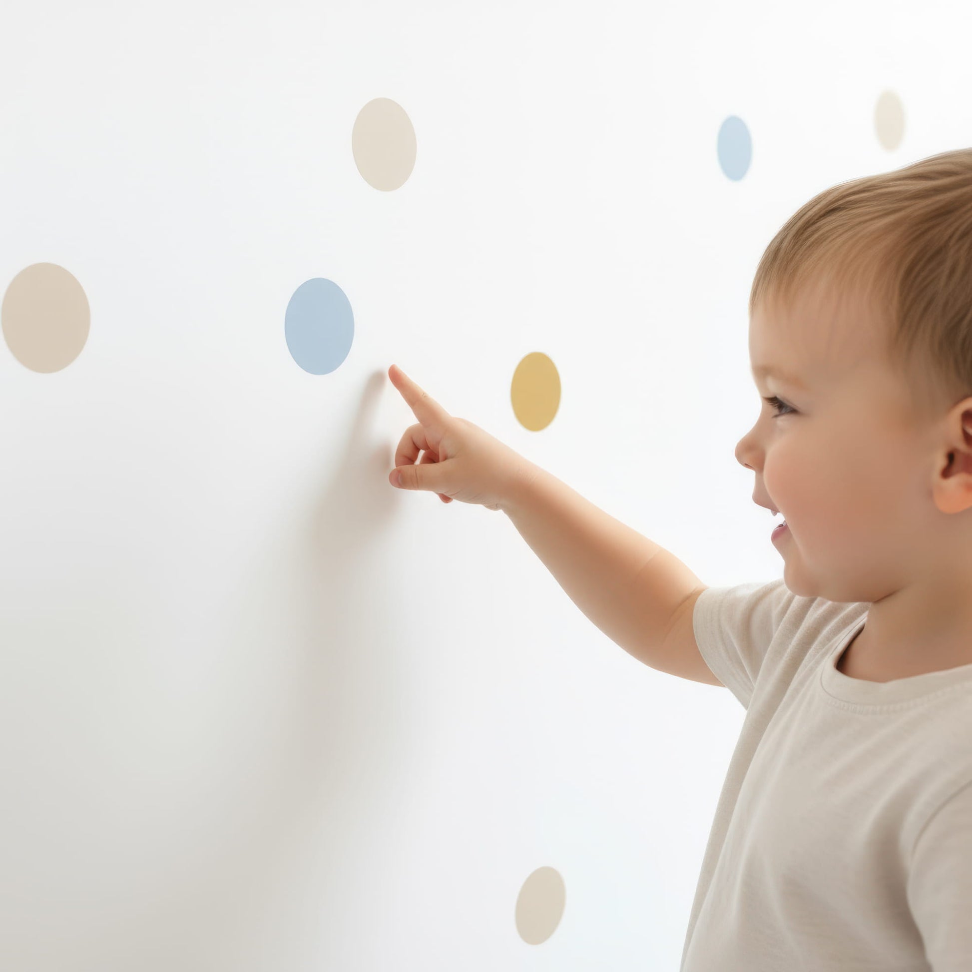 Un jeune enfant souriant pointe du doigt un sticker pois bleu doré sur un mur, mettant en avant la facilité d'utilisation de cette décoration murale pour chambre enfant et bébé.