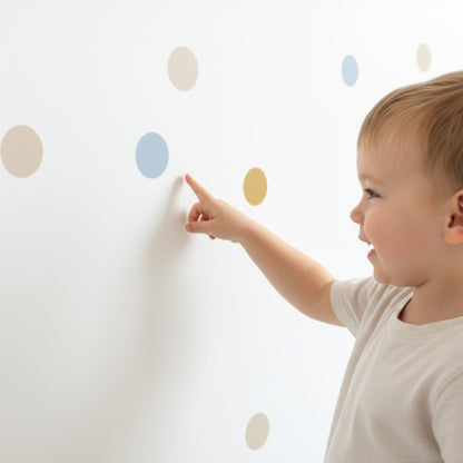 Un jeune enfant souriant pointe du doigt un sticker pois bleu doré sur un mur, mettant en avant la facilité d'utilisation de cette décoration murale pour chambre enfant et bébé.