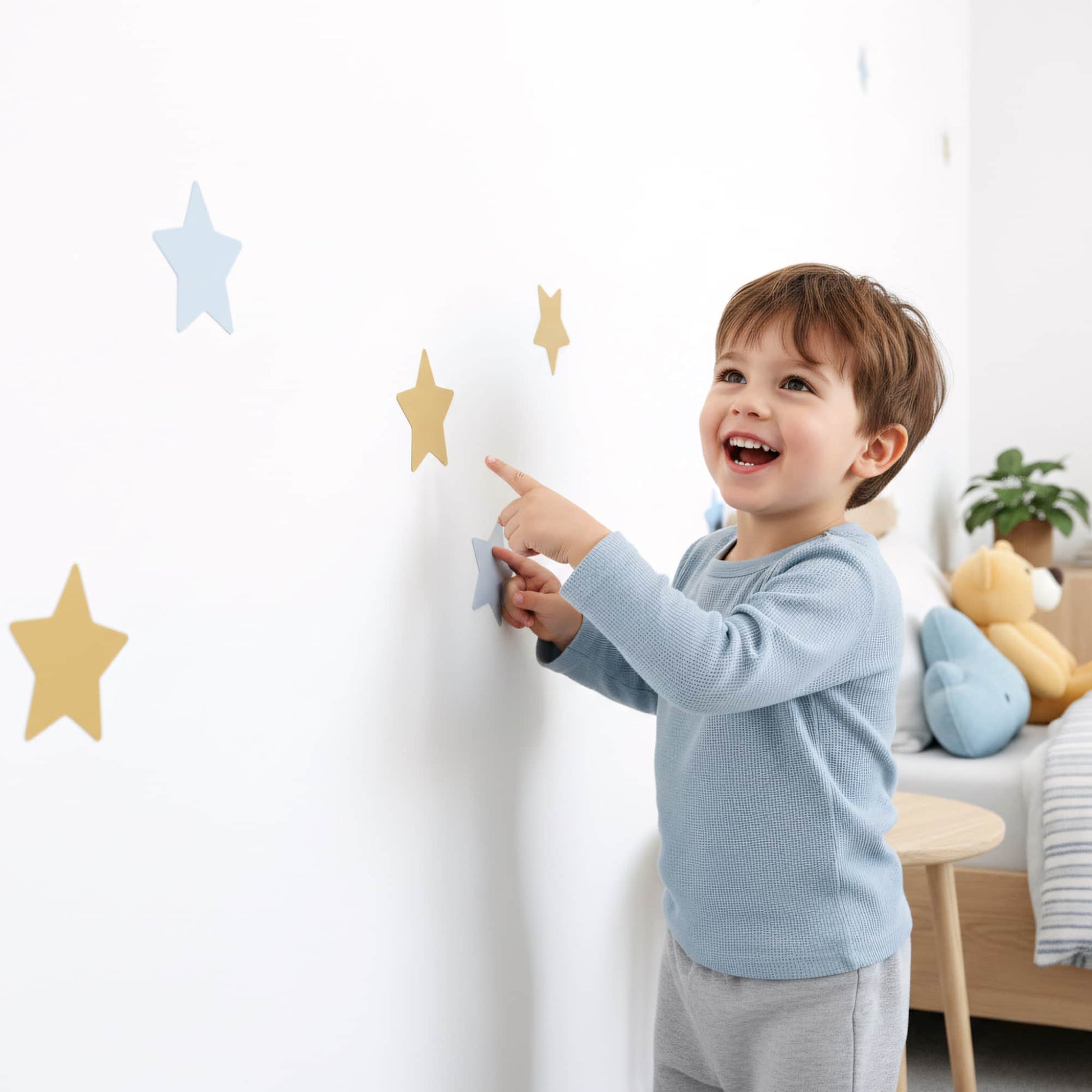 Un enfant colle lui-même un sticker étoile bleu doré sur le mur, illustrant la facilité d'utilisation de cette décoration murale dans une chambre de garçon.