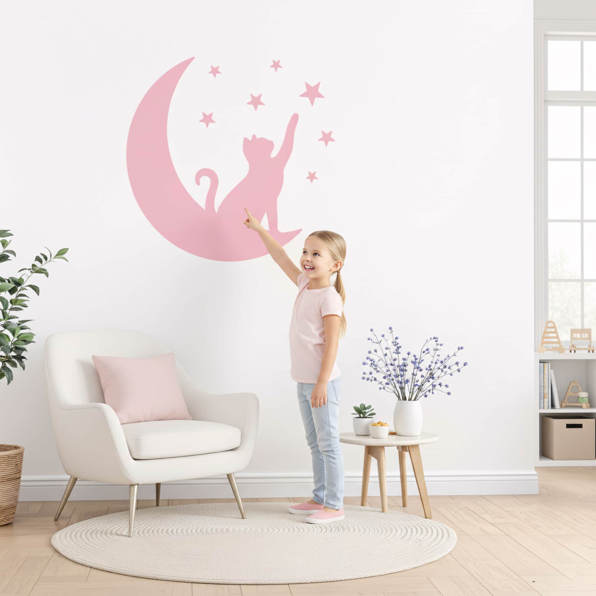 Fillette joyeuse montrant un grand sticker mural du Chat Lunaire rose sur un mur blanc, idéal pour la décoration murale d'une chambre enfant au Maroc.