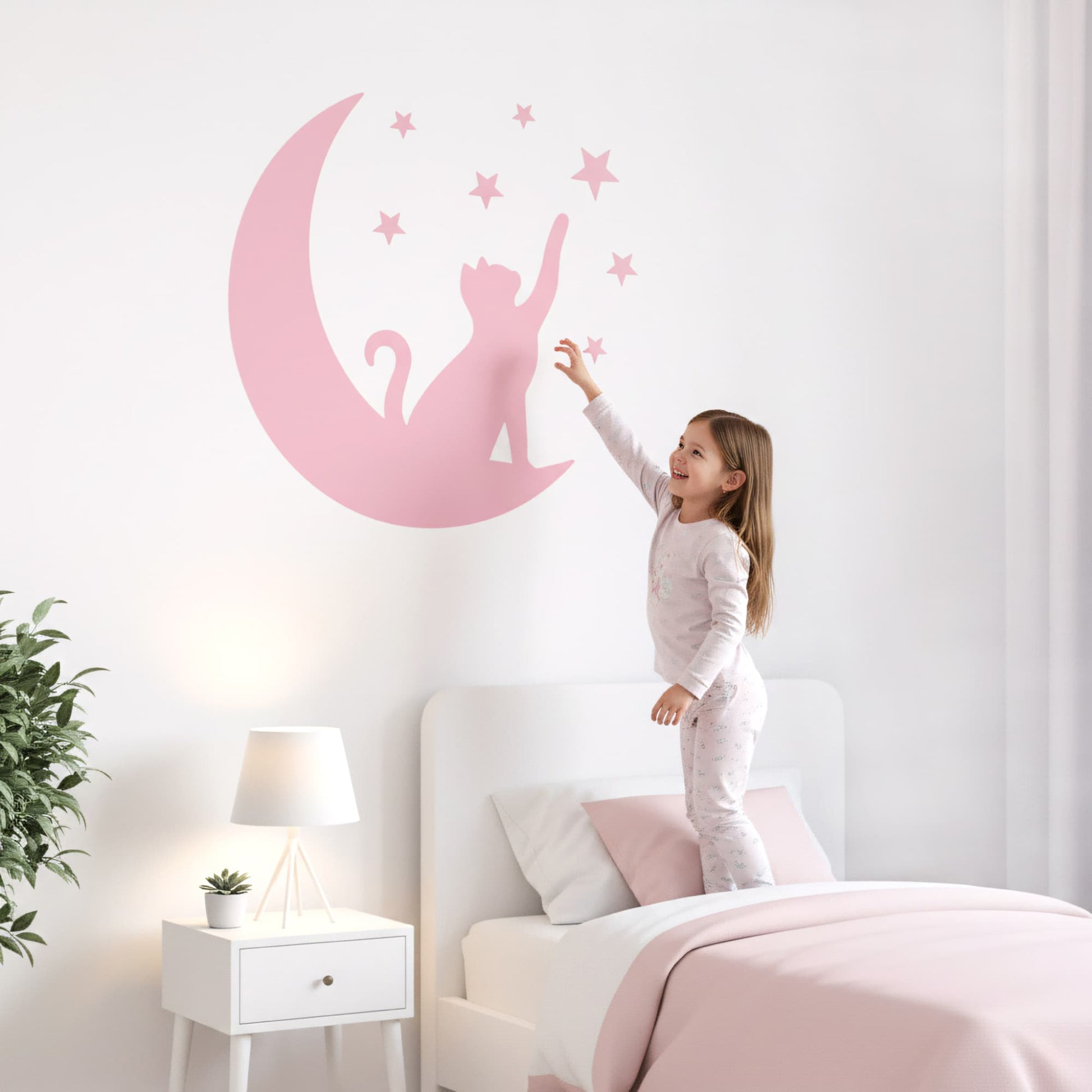 Une fillette se tenant debout sur son lit, jouant avec un grand sticker animaux du Chat Lunaire rose. Un élément décoratif pour une chambre enfant au Maroc.