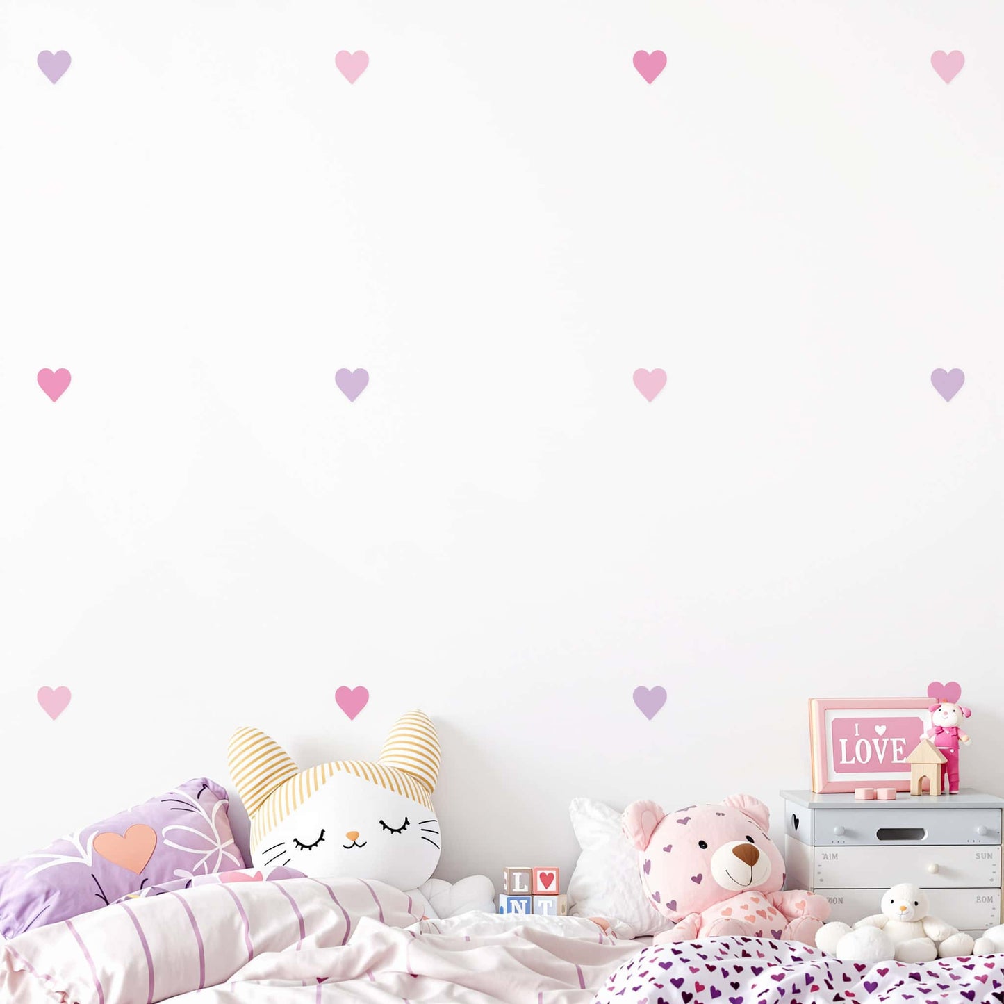 Un enfant joue paisiblement dans sa chambre décorée de stickers cœurs rose bonbon, une décoration murale qui rend l'espace plus chaleureux et joyeux.