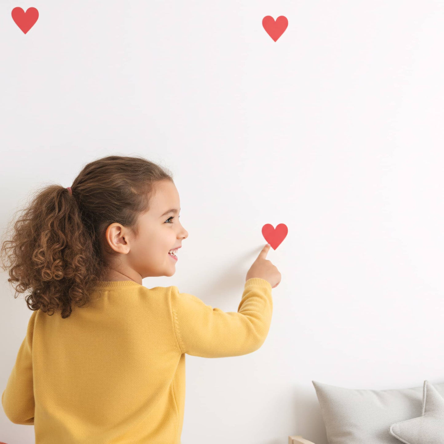 Une petite fille souriante colle un sticker cœur rouge amour, illustrant la facilité d'installation de cette décoration murale dans une chambre d'enfant au Maroc.