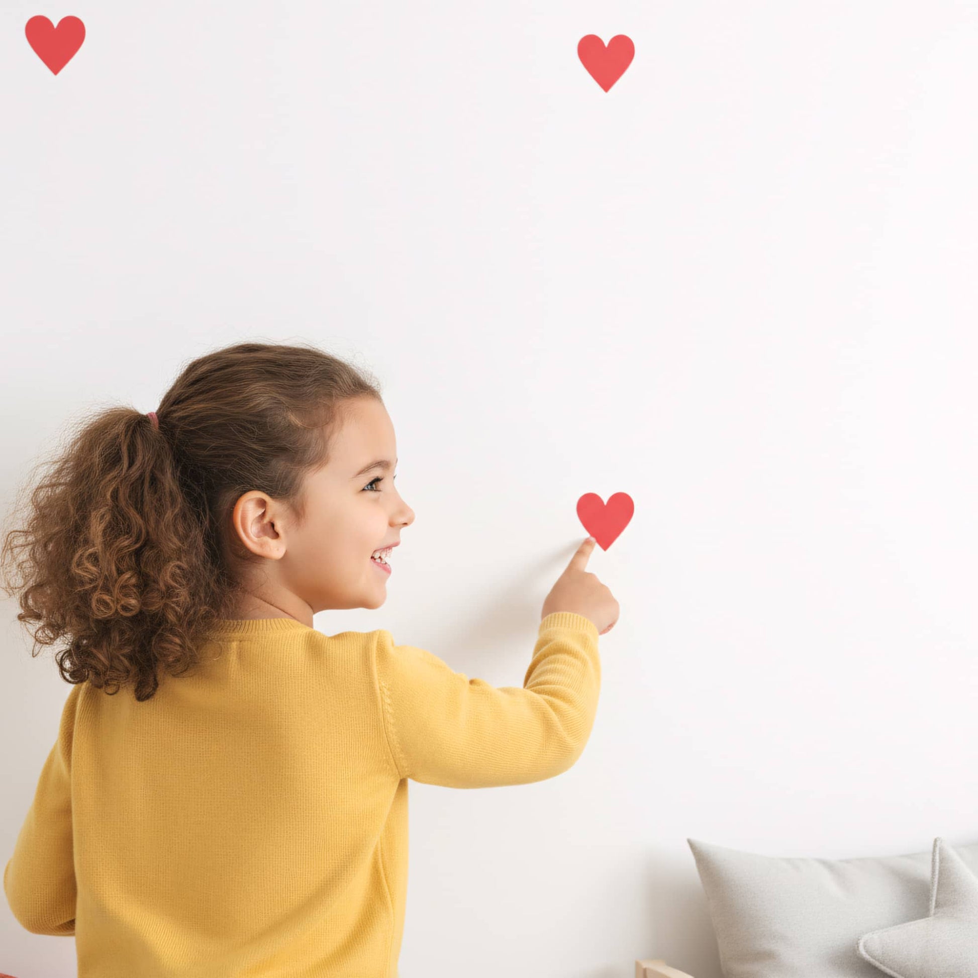 Une petite fille souriante colle un sticker cœur rouge amour, illustrant la facilité d'installation de cette décoration murale dans une chambre d'enfant au Maroc.