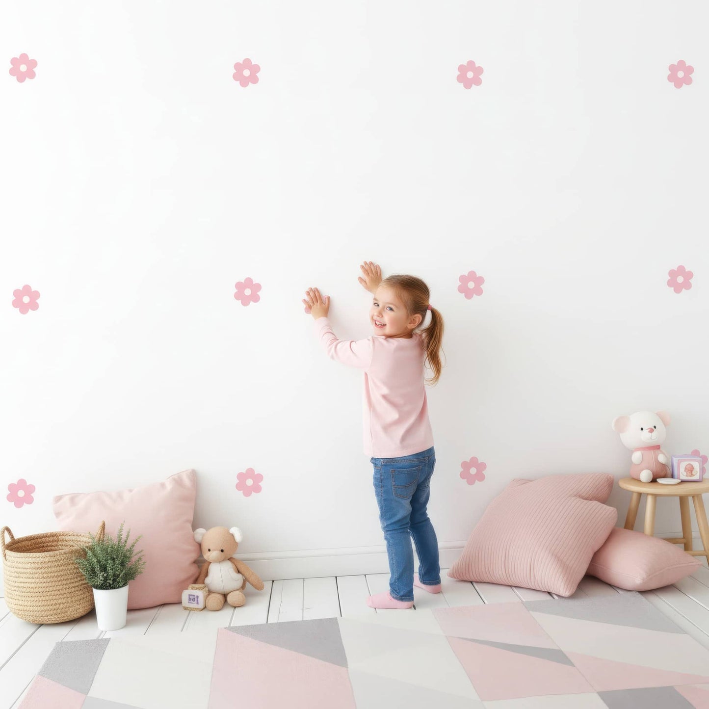 Une petite fille souriante colle des stickers fleurs marguerites roses sur le mur, montrant à quel point cette décoration murale est facile et amusante pour la chambre d'enfant.