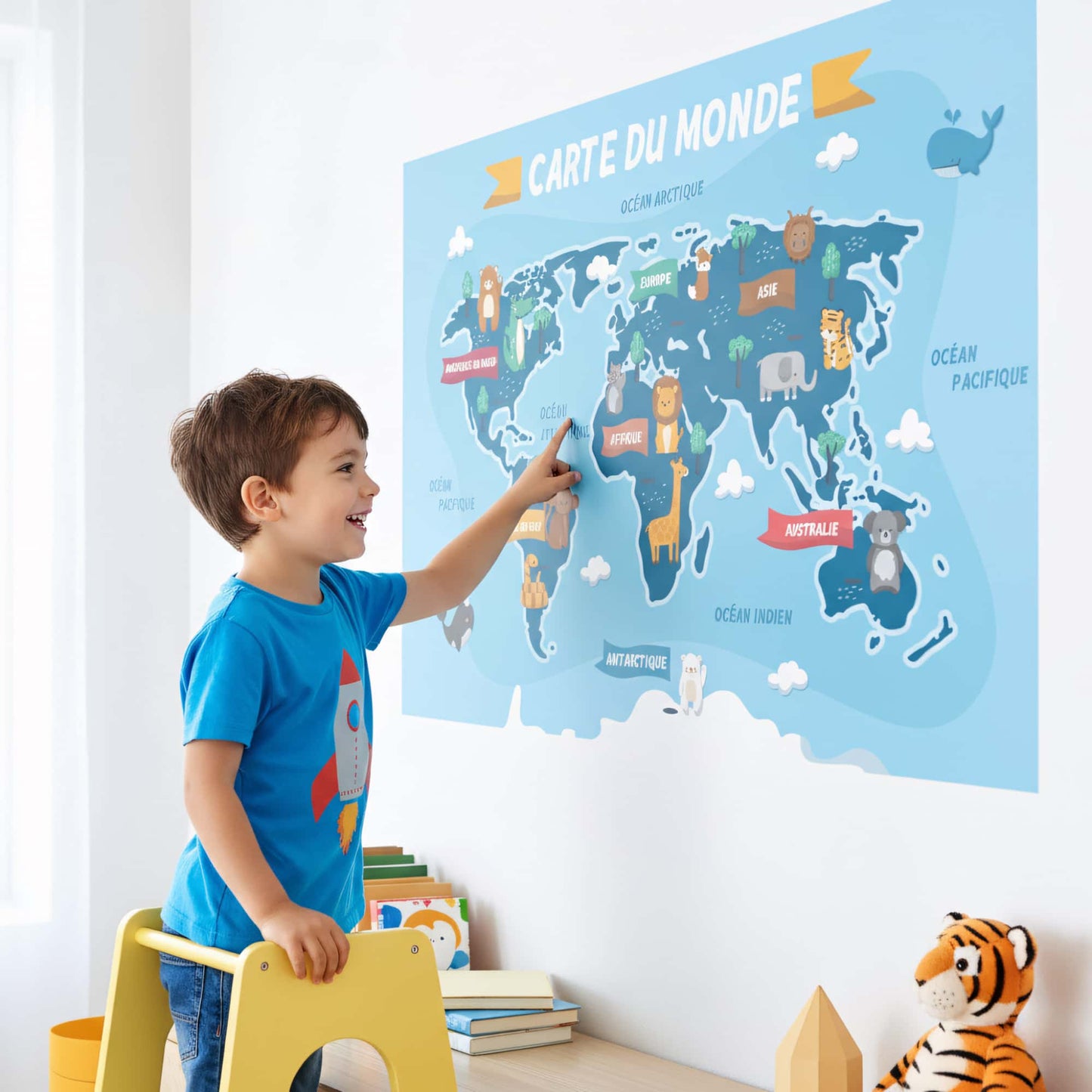 Enfant pointant du doigt un grand sticker mural carte du monde. Idée de décoration murale ludique pour chambre enfant au Maroc. Stickers éducatifs.