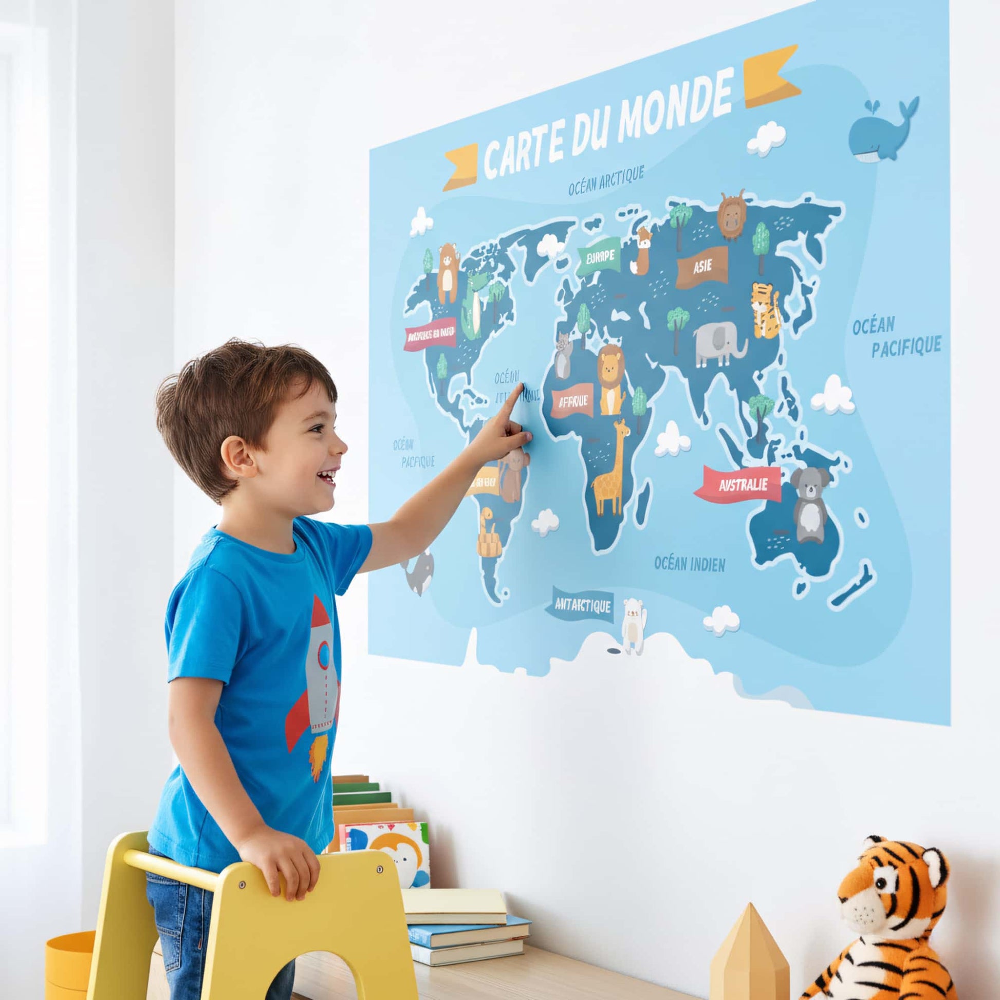 Enfant pointant du doigt un grand sticker mural carte du monde. Idée de décoration murale ludique pour chambre enfant au Maroc. Stickers éducatifs.