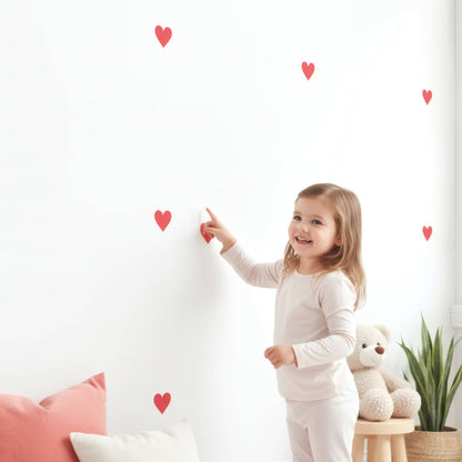 Une petite fille sourit en posant un sticker cœur rouge, illustrant la facilité d'installation de cette décoration murale dans une chambre d'enfant.