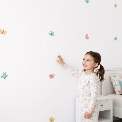 Petite fille souriante appliquant un sticker mural papillon. Décoration murale facile à poser pour une chambre d'enfant. Stickers de qualité au Maroc. Multicolore