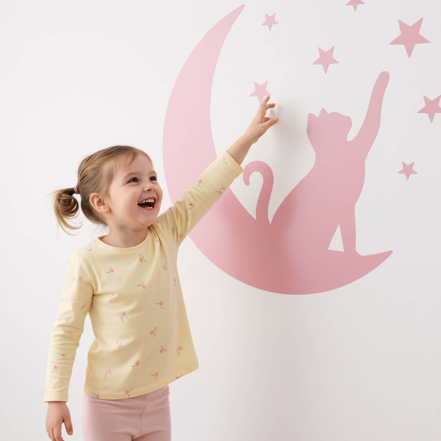 Jeune fille souriante tendant la main vers un sticker animaux de Chat Lunaire rose, un design ludique pour la décoration chambre enfant et bébé au Maroc.