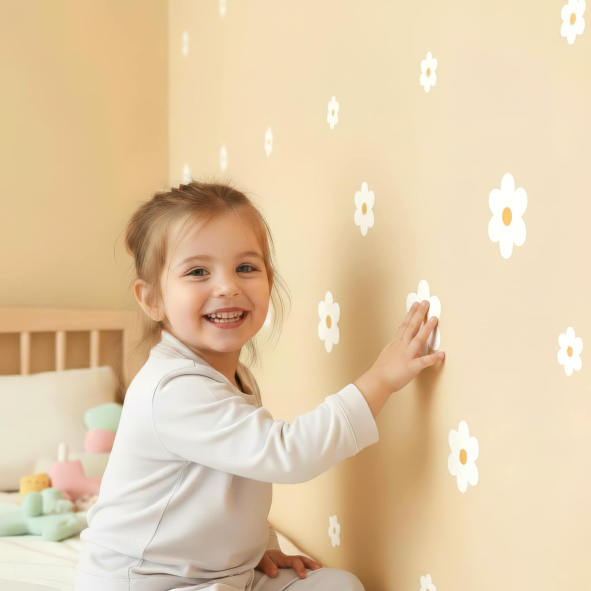 Une petite fille sourit en posant un sticker fleur marguerite blanche, montrant la facilité d'installation de cette décoration murale pour la chambre d'enfant.
